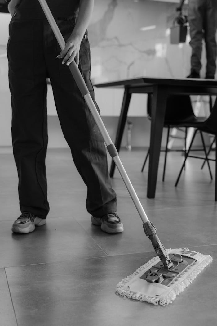 services-02 Monochrome image of a person mopping a tiled floor in an indoor setting.